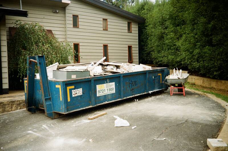 Blue hire skip full of household renovation waste sitting on a residential driveway