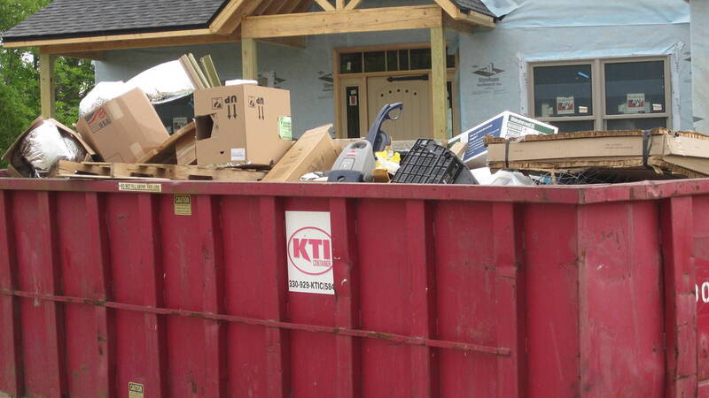 Red builders skip heaped with renovation packaging and household junk at a house site
