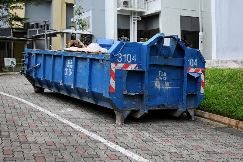 Large blue hook-lift skip bin placed on a paved residential driveway