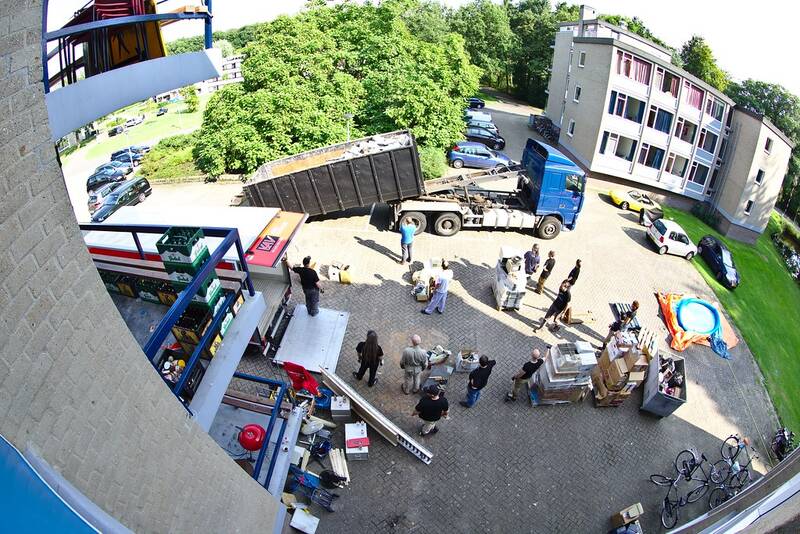Crew loading furniture and boxes into a waste container with a skip truck alongside