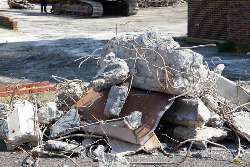 Concrete rubble with reinforcing wire at a demolition site with an excavator behind
