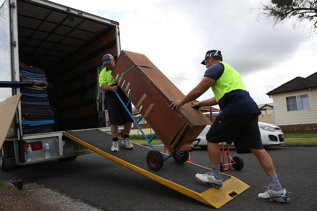 Removal worker carrying a labelled moving box up a truck ramp during a house clearance