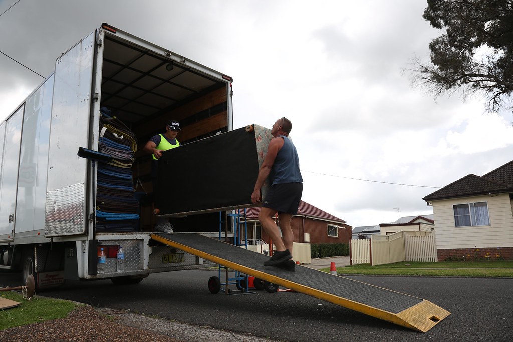 Two removal workers loading a lounge suite couch up a ramp into a truck during an estate clearance