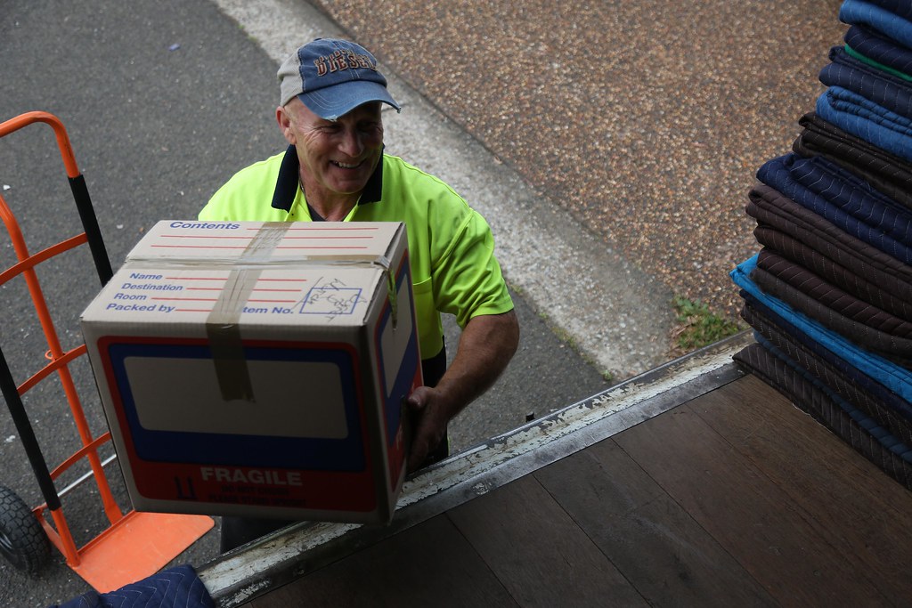 Two workers wheeling a cabinet on a trolley up a ramp into a truck — the crew loads for you